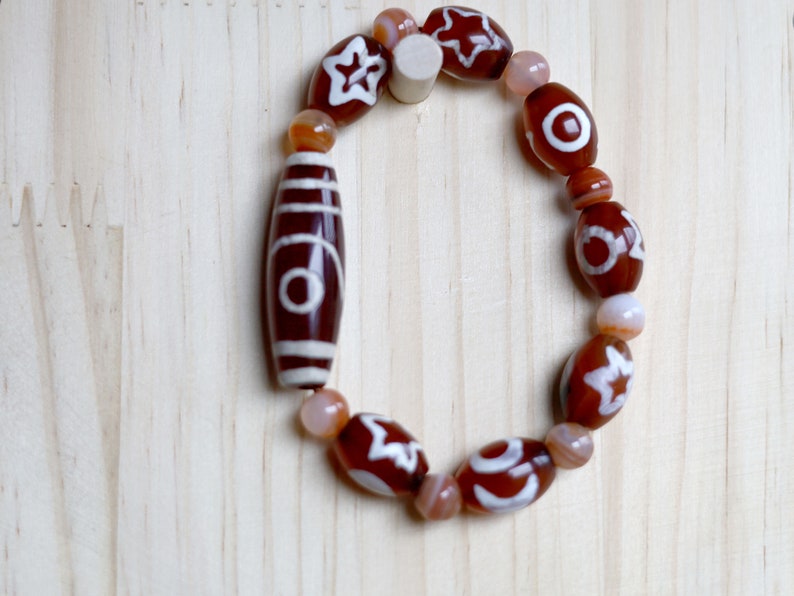 Two-eye dZi bead with Universe Dzi Bead | Sun/Moon. The sun, moon, and star painted on this Dzi bead represent this universal life energy.