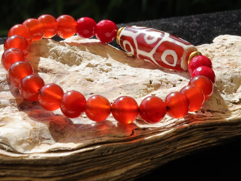 This precious Nine Eyed DZI bead is strung with natural red Carnelian. And Faceted Red Coral beads..