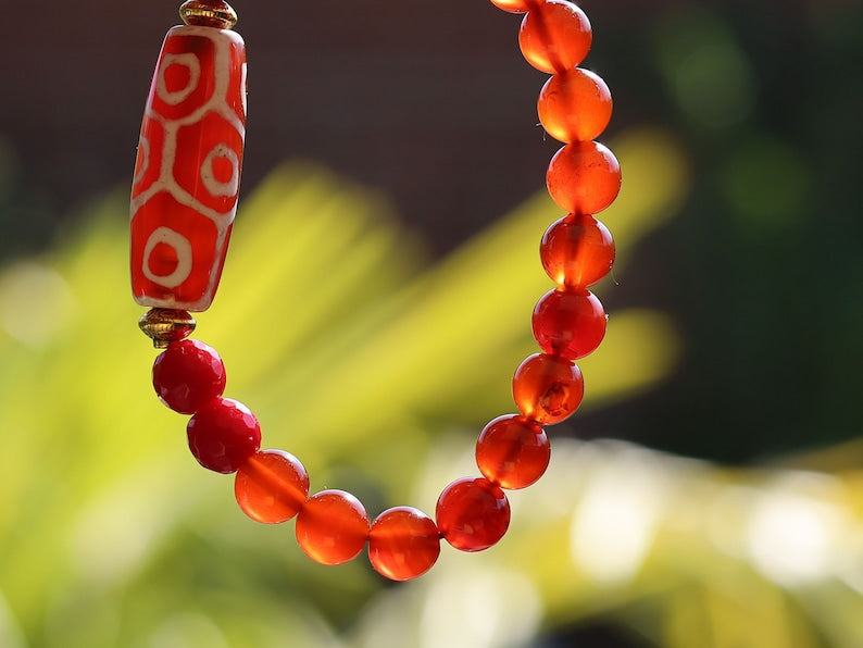 This precious Nine Eyed DZI bead is strung with natural red Carnelian. And Faceted Red Coral beads..