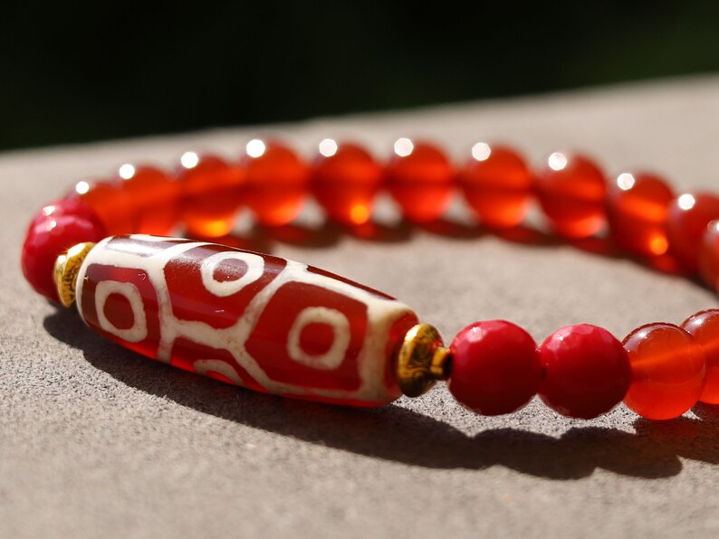 This precious Nine Eyed DZI bead is strung with natural red Carnelian. And Faceted Red Coral beads..