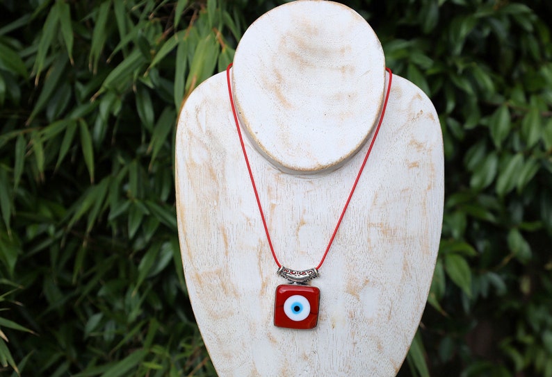 A red evil eye pendant carries with it the ancient belief in the protective power of the "evil eye," a symbol meant to ward off harm and malevolent energies directed towards the wearer.